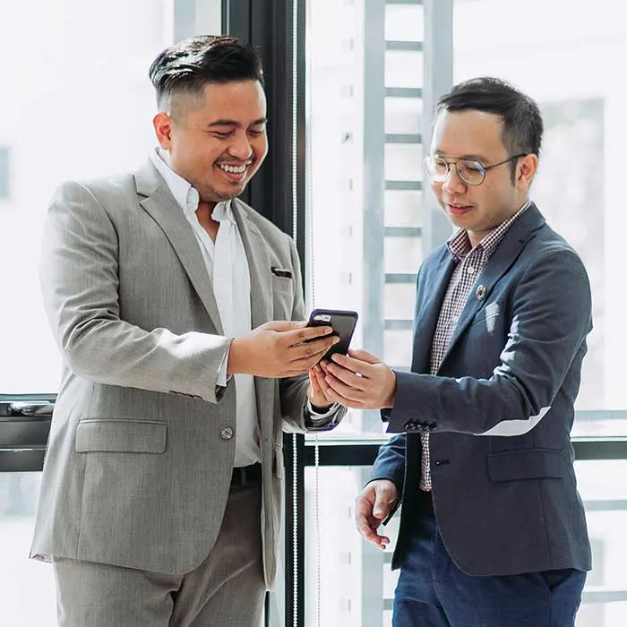 Two colleagues in suits looking at a phone in a bright office